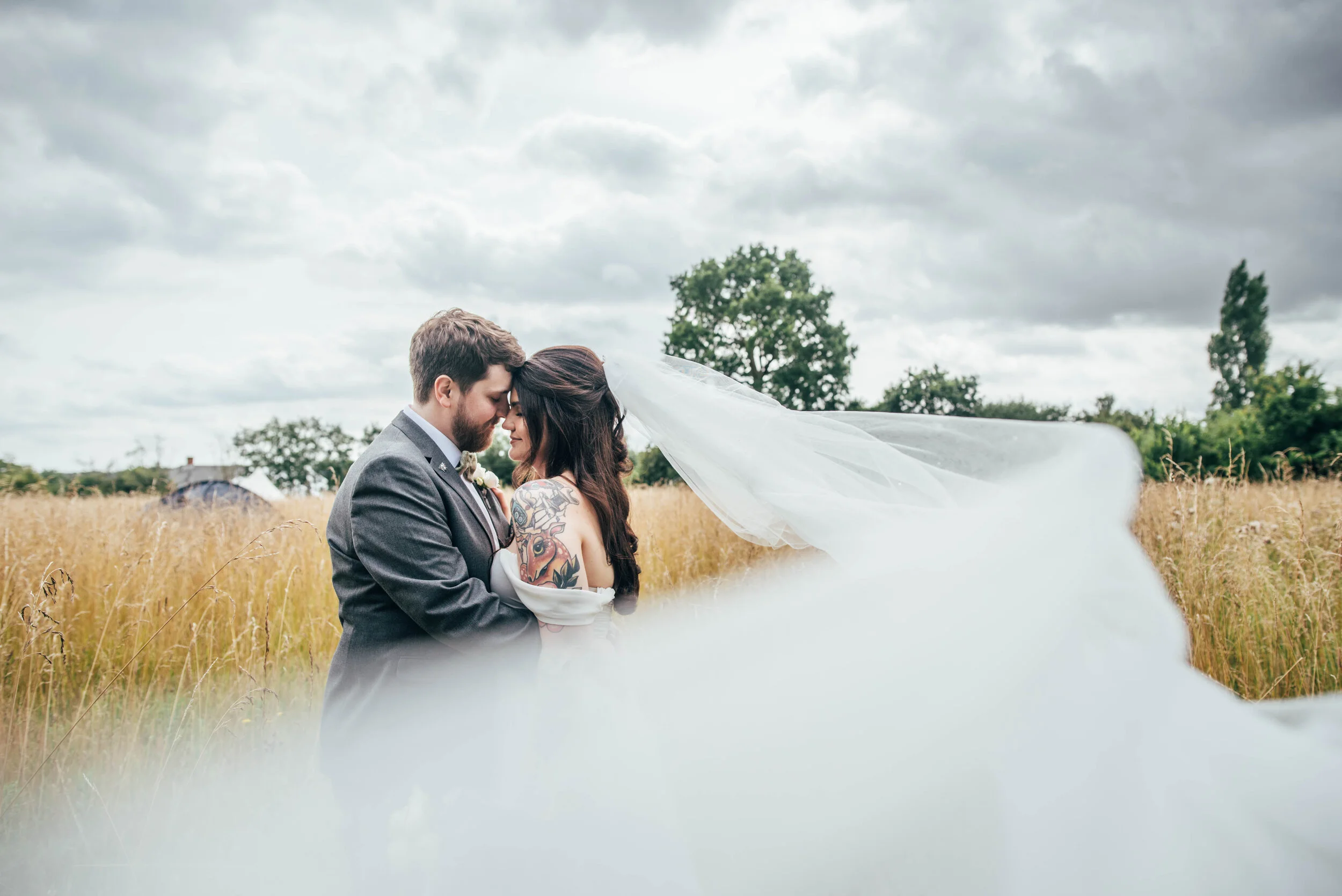 Bride & Groom with blowing veil in field at Farm Wedding. Essex Documentary wedding photographer. Three Flowers Photography