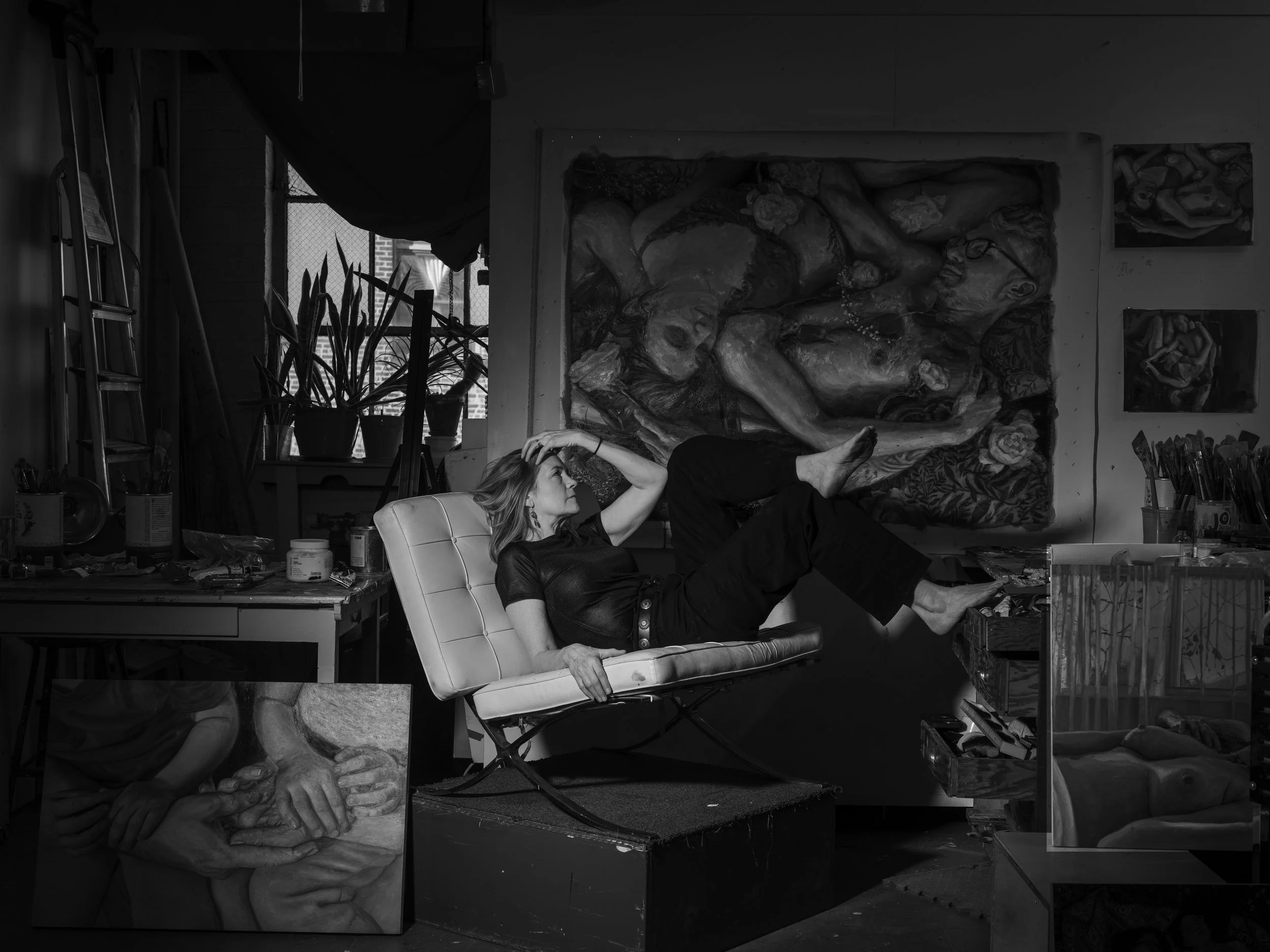 Portrait of Michelle Doll, a contemporary oil figure painter who focuses on themes of intimacy, femininity, family, and affection. She poses on her studio alongside a variety of original work by her side.
