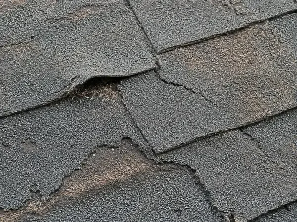 Close-up of curling and cracked asphalt roof shingles showing signs that roof needs to be replaced