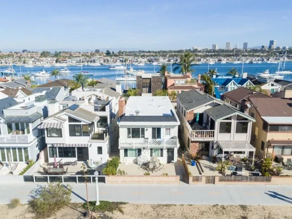 Waterfront homes overlooking a marina with boats and a coastal skyline on a sunny day.