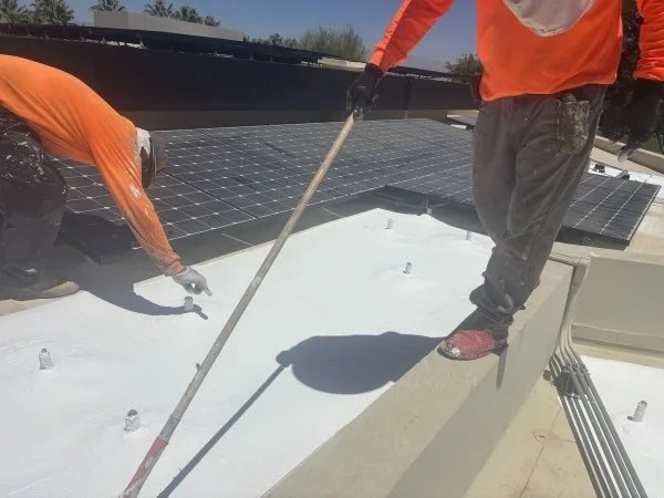 Roofers applying reflective white coating around rooftop solar panels.