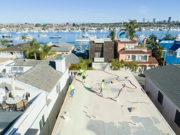 Foam roofing installation underway on waterfront flat roof residence.