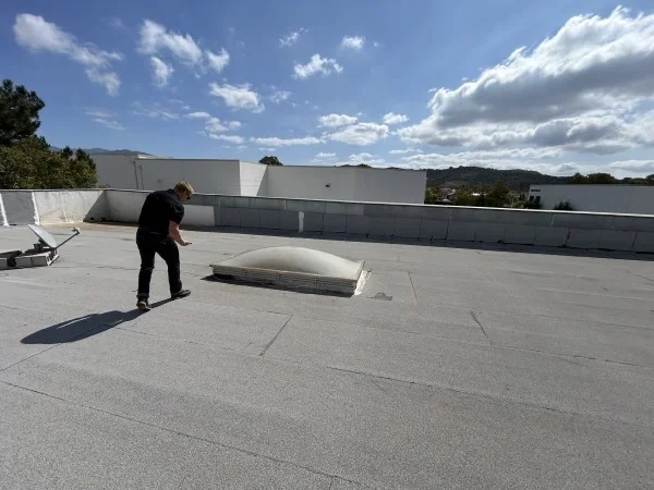 Roofer inspecting commercial flat roof around rooftop skylight