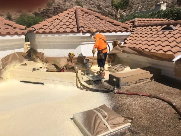 Roofer applying spray foam coating around residential roof details.