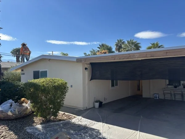 Roofer working on residential flat roof replacement above carport.