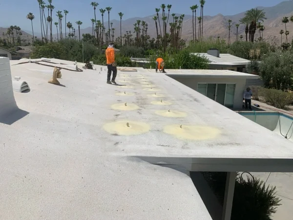 Roofers applying spray foam around multiple roof penetrations