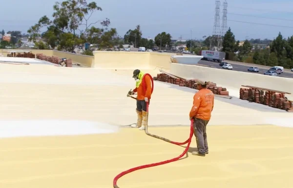 Contractors applying spray foam insulation across commercial flat roof.