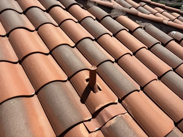 Plumbing vent flashing installed through clay tile residential roof.