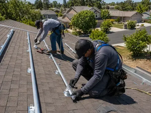 Licensed roofing crew installing solar panel racking brackets on residential shingle roof