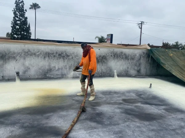 Roofer spraying foam coating over prepared commercial flat roof