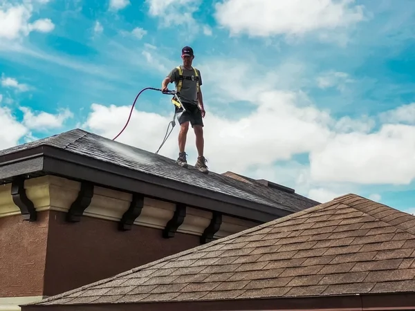 Roofer applying roof rejuvenation treatment to asphalt shingles