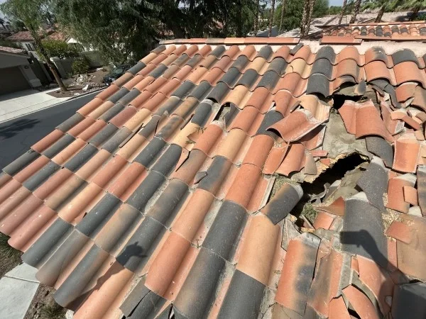 Broken clay roof tiles exposing damaged roofing underlayment beneath.