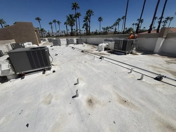 White commercial roof coating with rooftop HVAC and vent pipes.