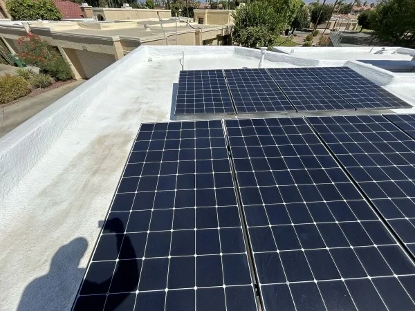 Solar panels installed on reflective white flat residential roof.