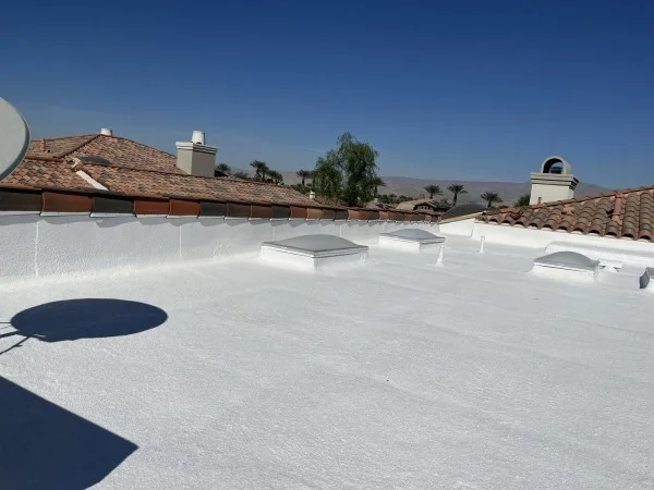 Fresh white foam roof coating surrounding residential skylights.