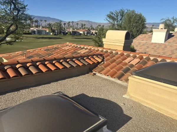 Clay tile roof beside flat roofing system with skylights.