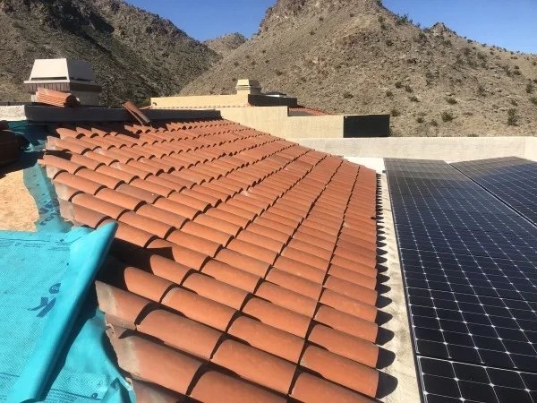 Clay tile roof beside solar panels in desert mountain landscape.
