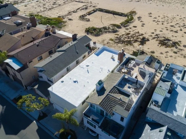 Aerial view of a flat white roofing system installed on a coastal residential property.