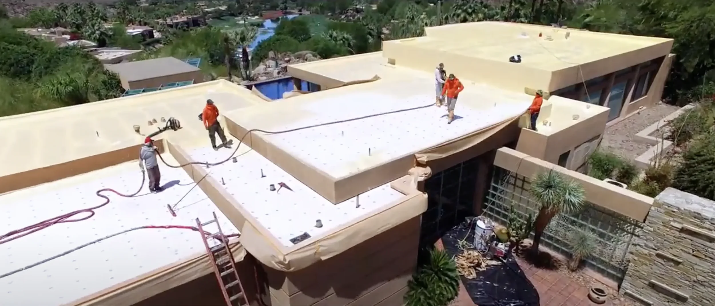 Roofing crew applying spray foam to a residential flat roof