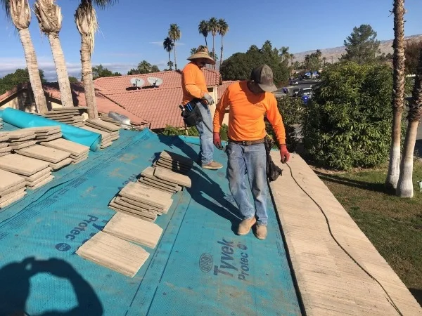 Roofing crew installing underlayment beneath concrete roof tiles