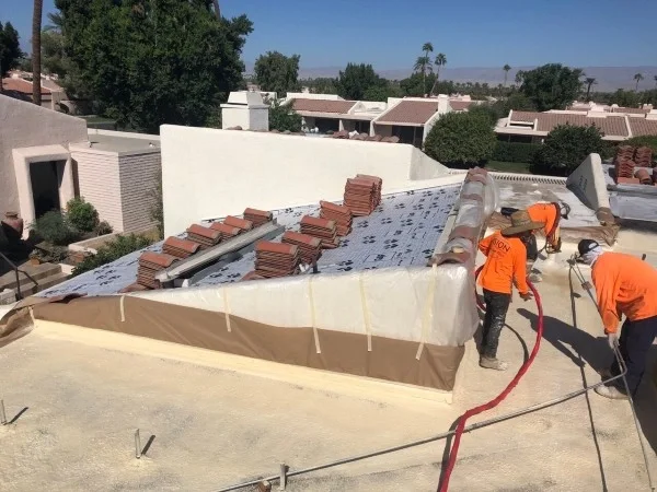 Crew applying spray foam around residential tile roof transition.