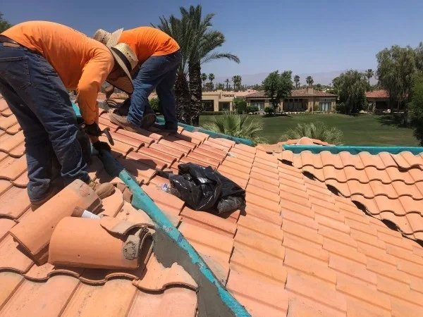Roofers repairing residential clay tile roof under sunny skies