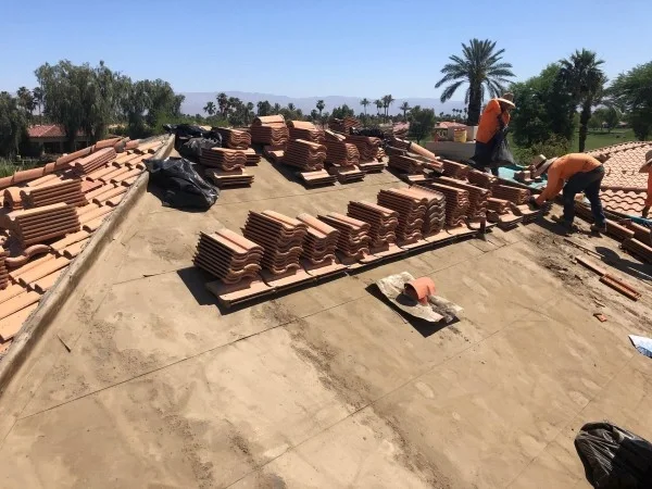 Roofers replacing clay tiles across residential roofing system