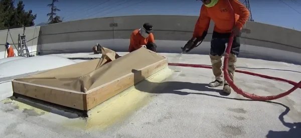 Applying spray foam waterproofing around commercial roof skylight
