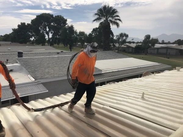 Contractor applying spray foam roofing on corrugated metal roof.