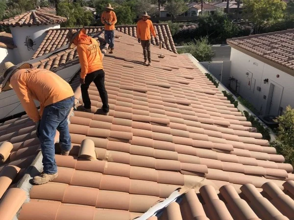 Roofing crew installing replacement clay tiles across residential roof.