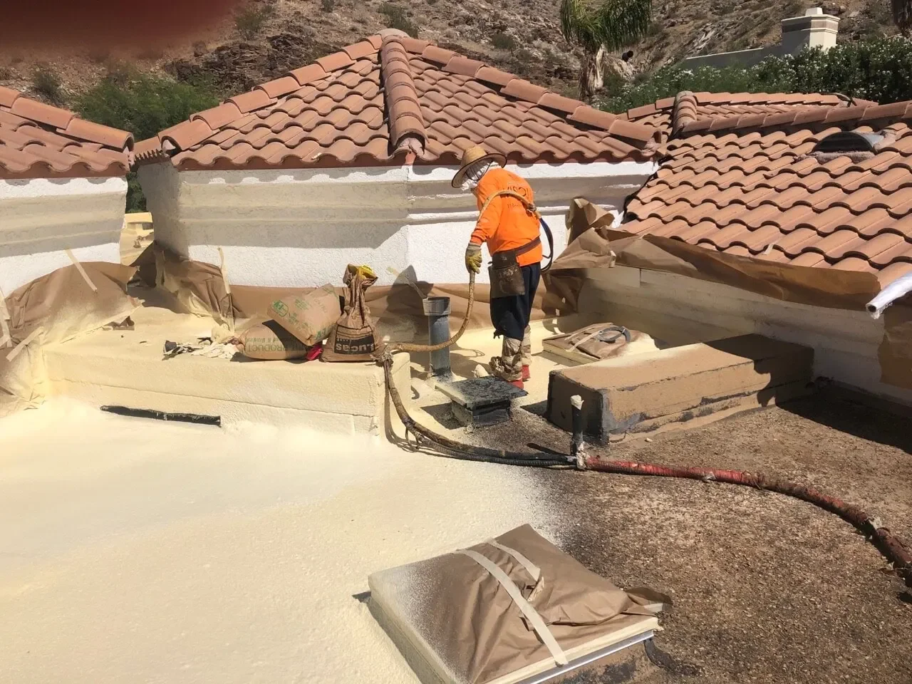Roofer applying spray foam coating around a tile roof