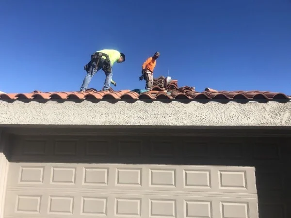 Roofers replacing broken clay tiles along residential roof ridge.