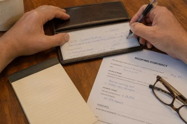Writing small deposit check beside roofing contract