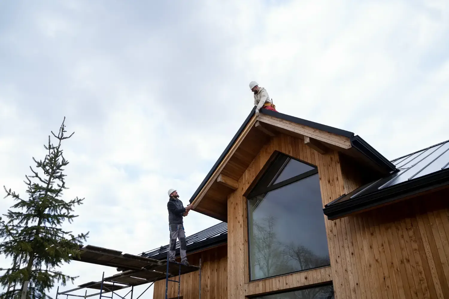 Roofers installing standing seam metal roof on modern home