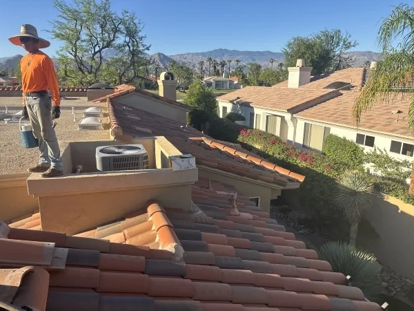 Roofer inspecting completed tile roofing beside residential flat roof.