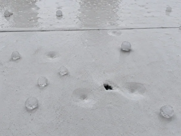 Hail damage and a puncture on a white commercial roof membrane after a storm
