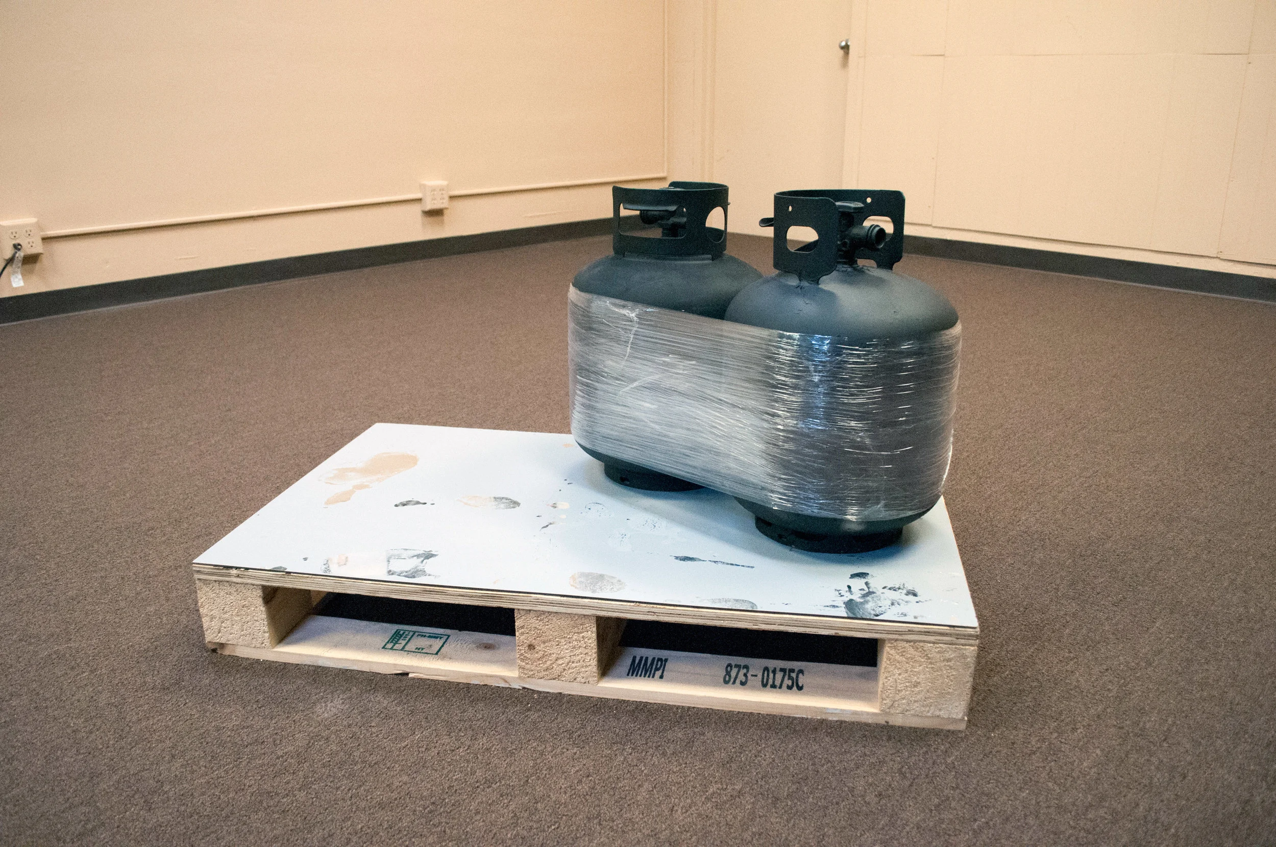 From the Beginning We Always Knew We Weren’t Gonna Make It (After Brancusi’s Kiss), 2016, 2 propane cylinder tanks, clear plastic stretch wrap, matte black spray paint, recycled wood pallet.