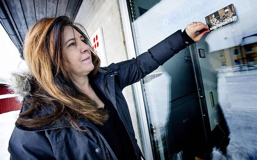 Carinne Sjoberg peeling off a sticker that neo-Nazis left on the door of what used to be the Jewish community center of Umea, Sweden. (Photo Courtesy of Sjoberg/via JTA)