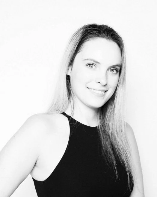 Black and white portrait of a young woman with long hair, smiling, wearing a sleeveless top.