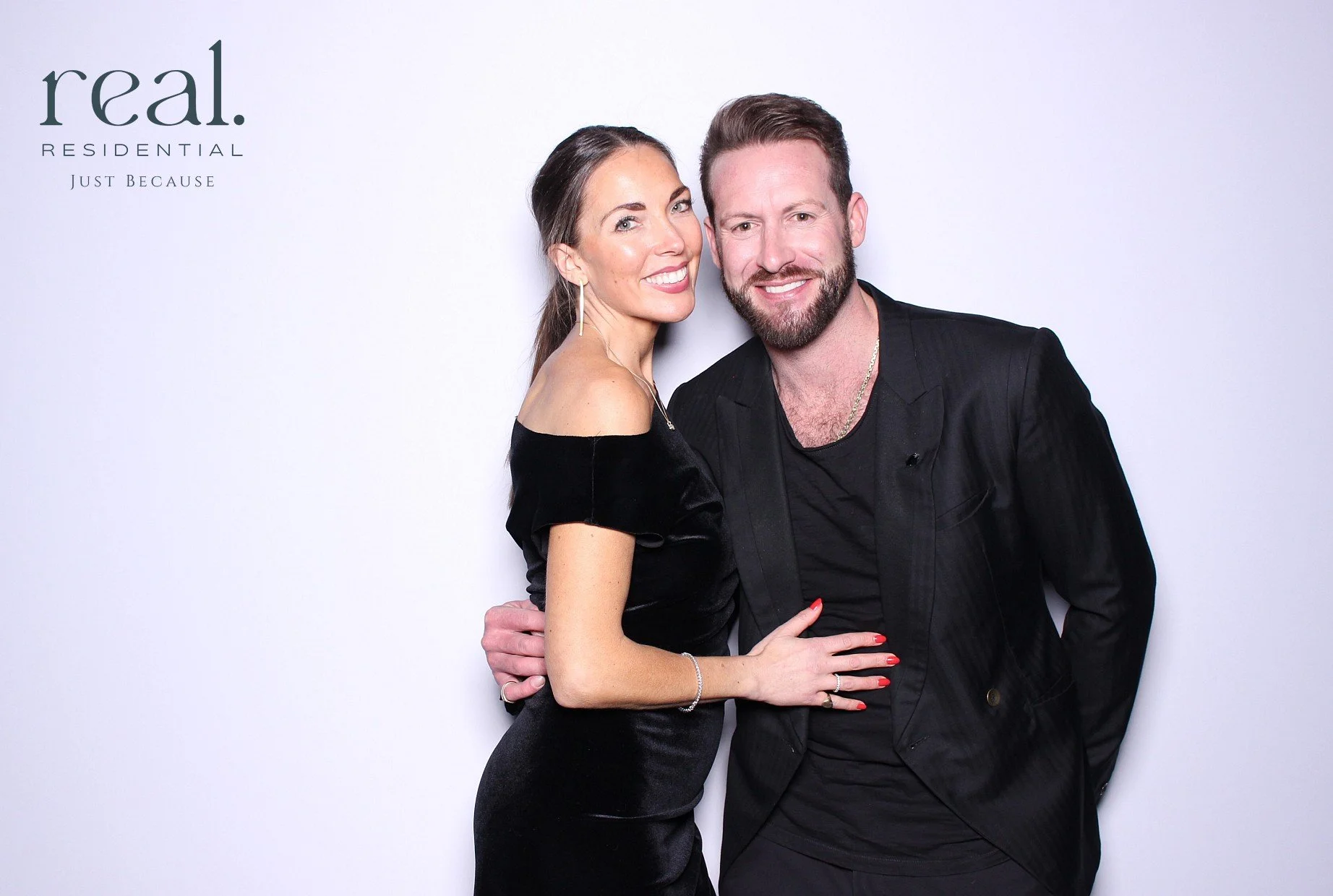 A smiling woman and man in black clothing standing close together against a white background with the words 'real. residential just because' in the upper left corner.