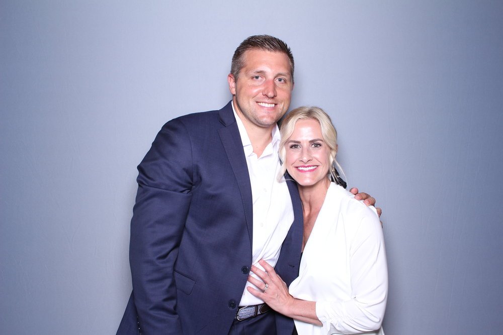A man and a woman dressed in business attire smiling and posing together against a plain gray background.