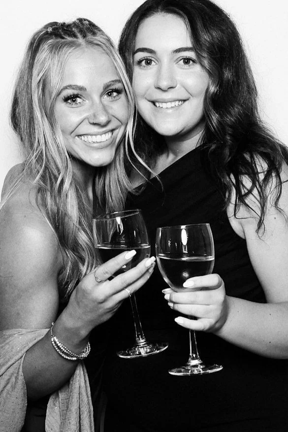Two women smiling and holding glasses of white wine, celebrating together.