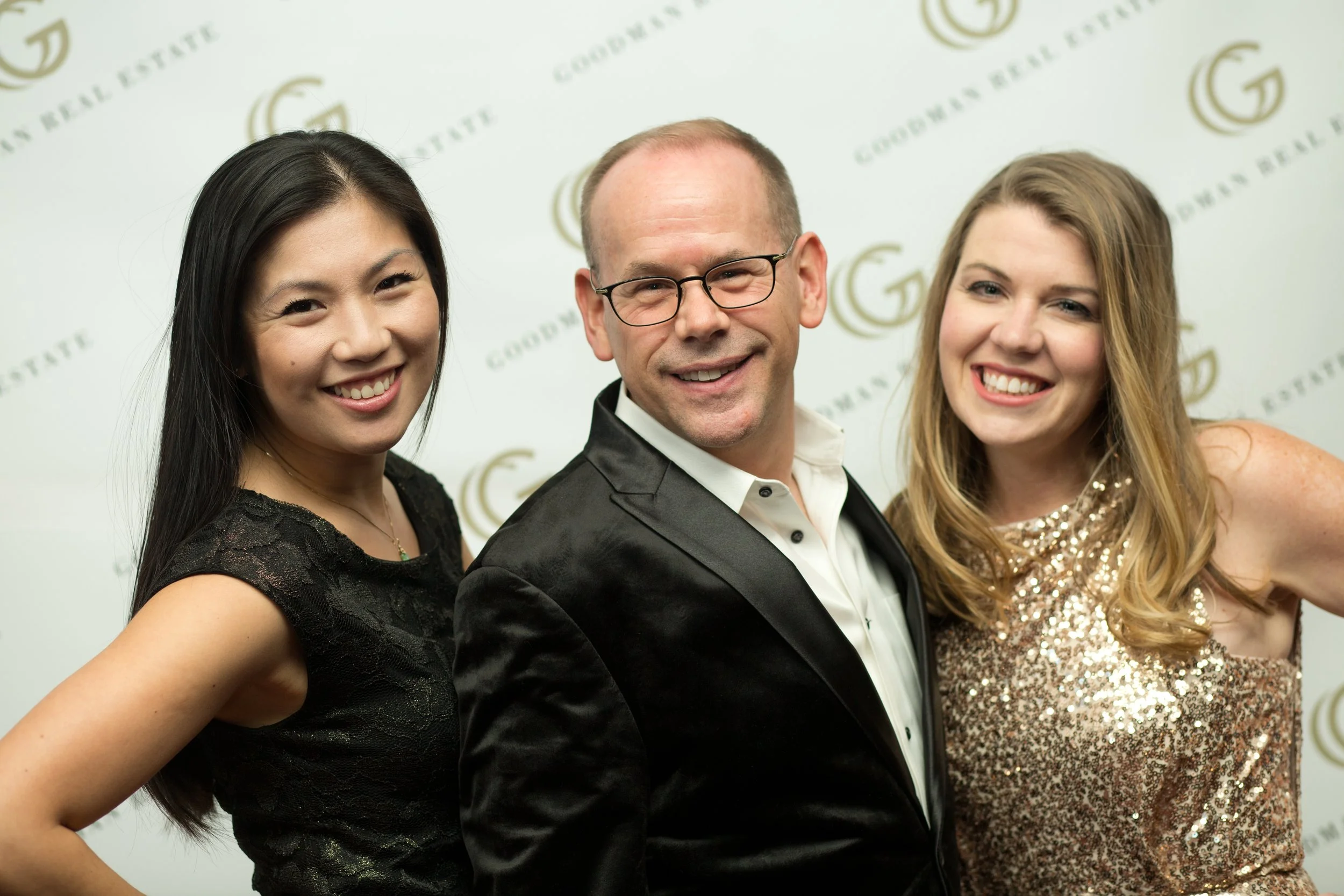 Three smiling people dressed in formal attire posing at an event with a backdrop that reads "Gordon Real Estate."