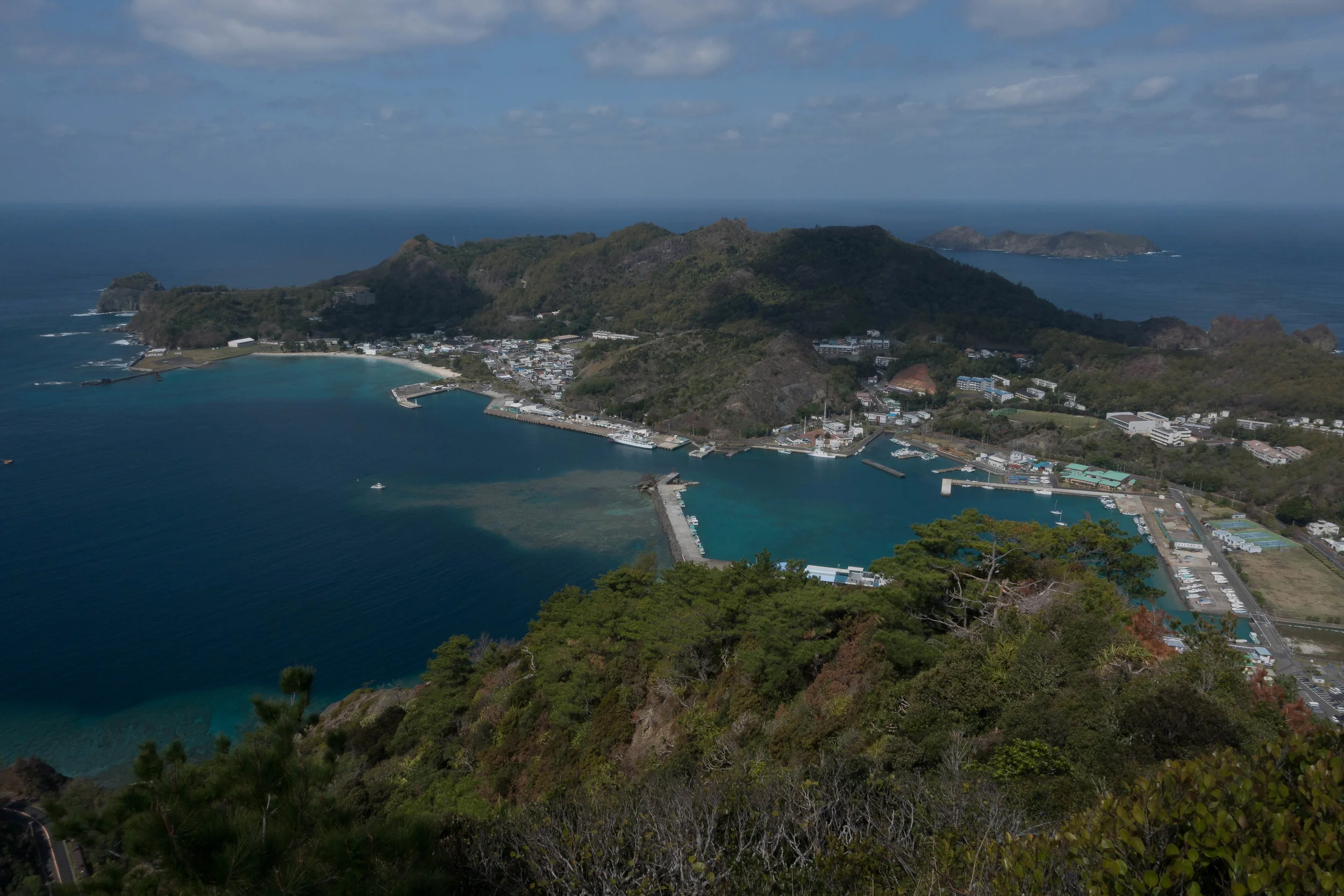 Chichijima from Asahi Mt. Tumbleweed is in the inner harbor, on the right, against the long pier that is capped with a breakwater running toward camera.