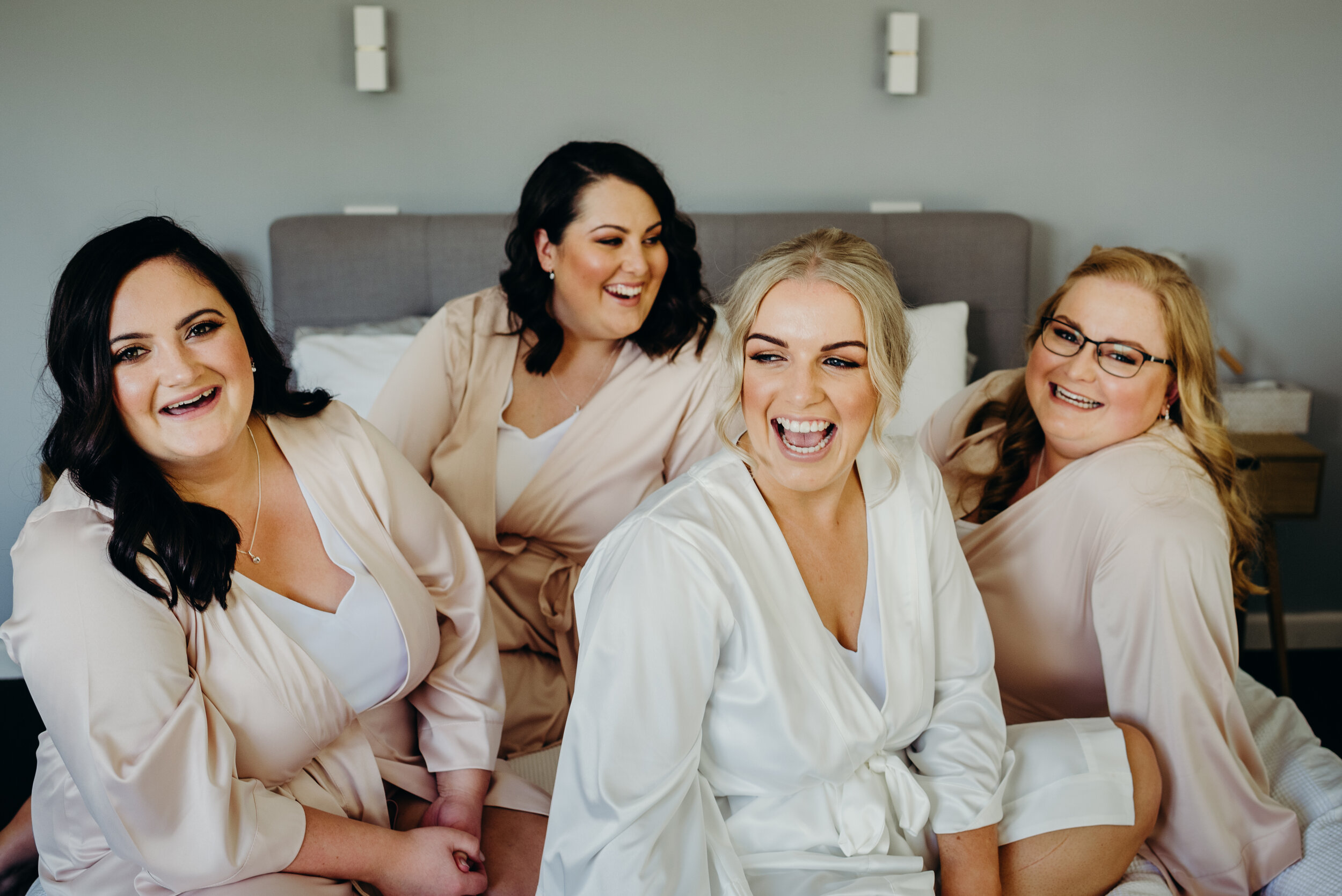 Bridesmaids sitting on a bed laughing. 