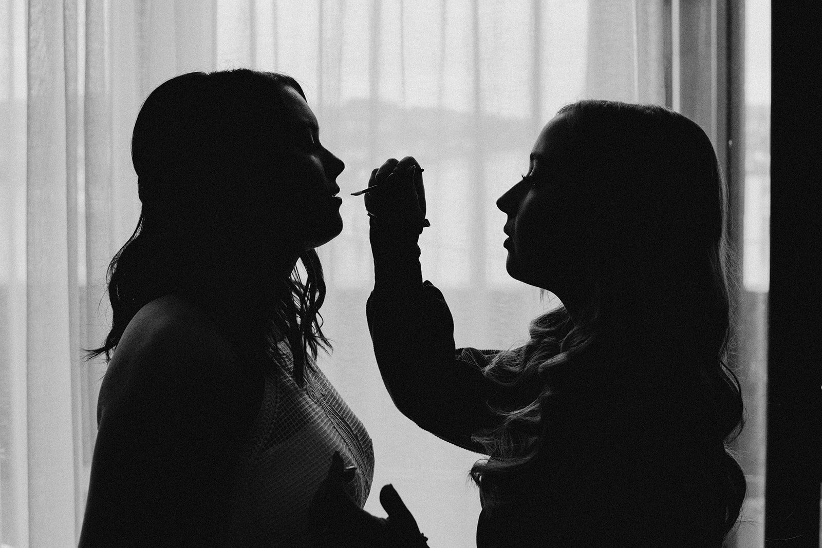  Shilouette of a bridesmaid putting lipstick on the bride, black and white. 