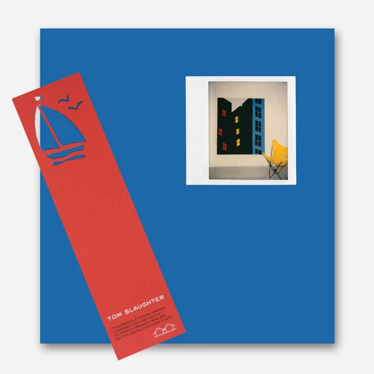 The Tom Slaughter book cover is solid blue with the image of a Polaroid photograph in the top-right corner. A red bookmark with a cutout sailboat shape sits on top of the book.