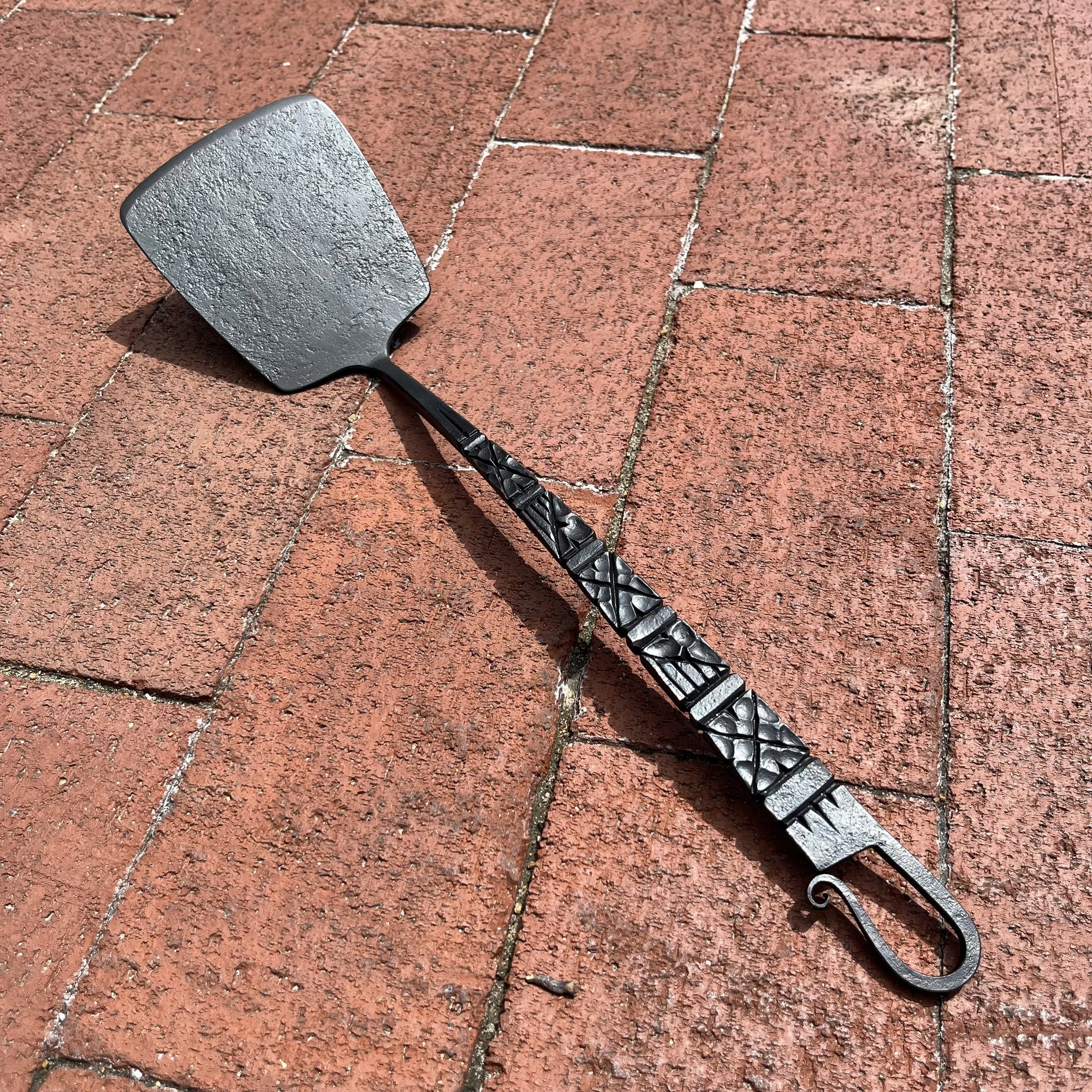 A handmade spatula with fine chisel work decorating the handle by Smith Shop in 2023.