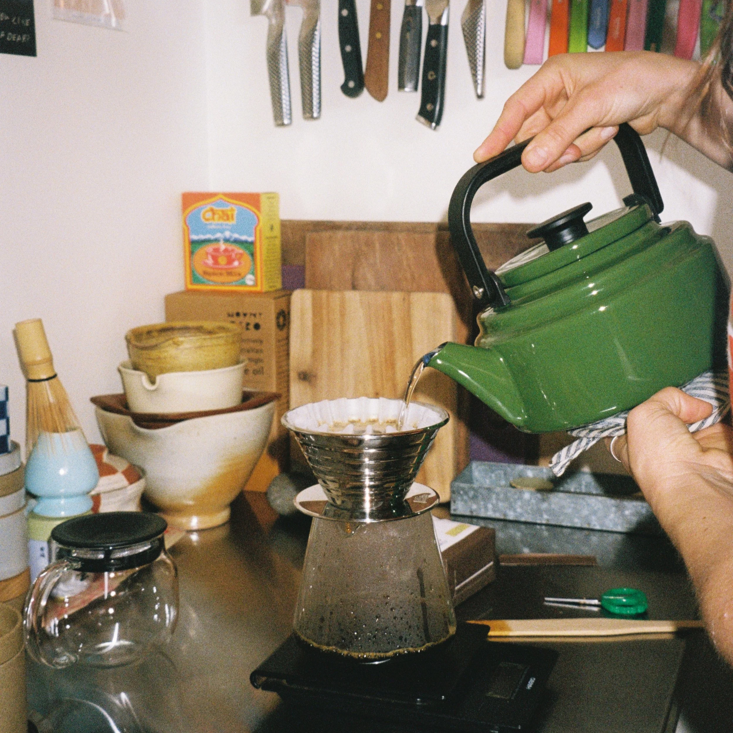 A person pouring from a green kettle into a Kalita Wave filter coffee dripper at home, showing the brewing style featured in our Melbourne coffee subscription.