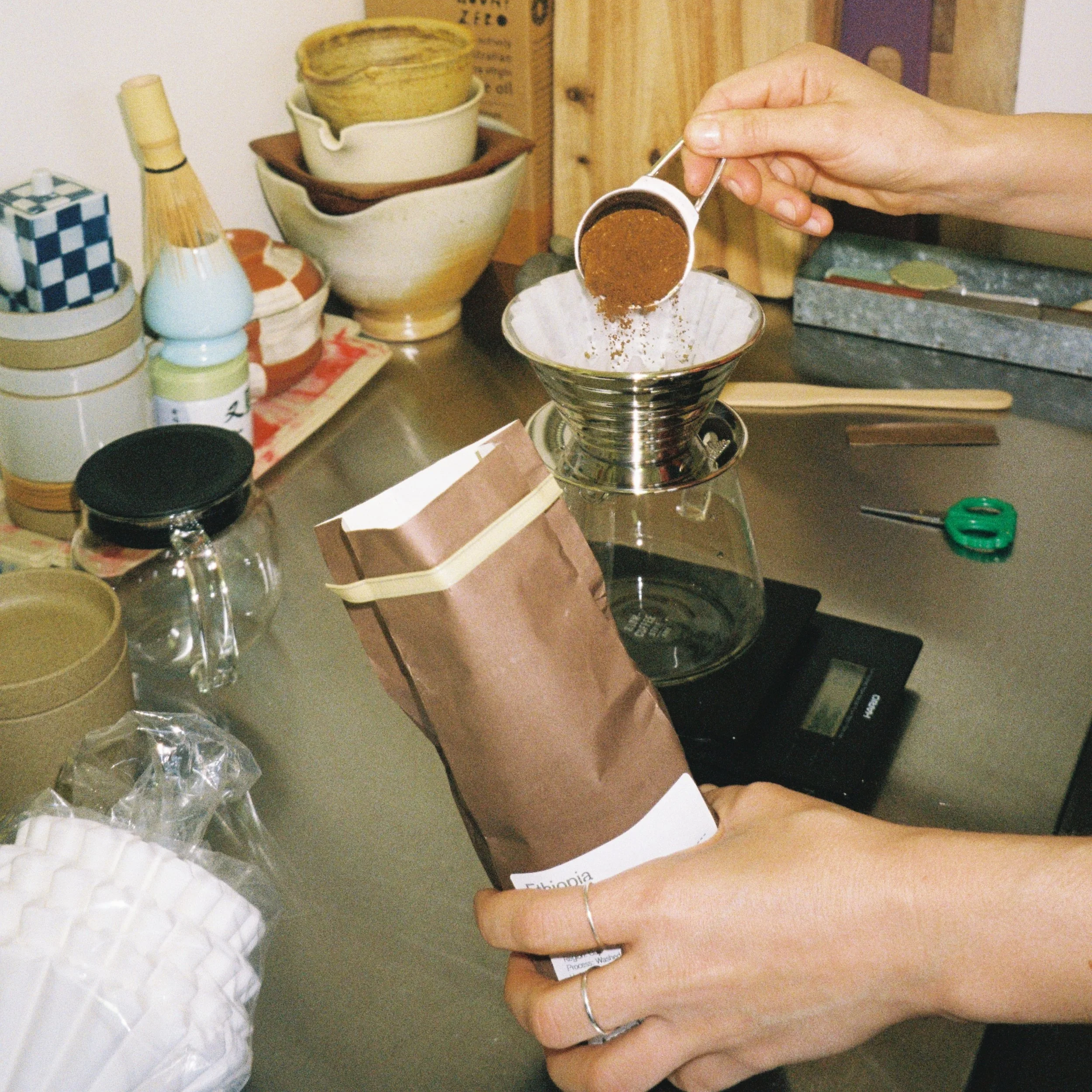A person scooping ground coffee into a steel Kalita Wave filter coffee dripper at home, showing the brewing style featured in our Melbourne coffee subscription.